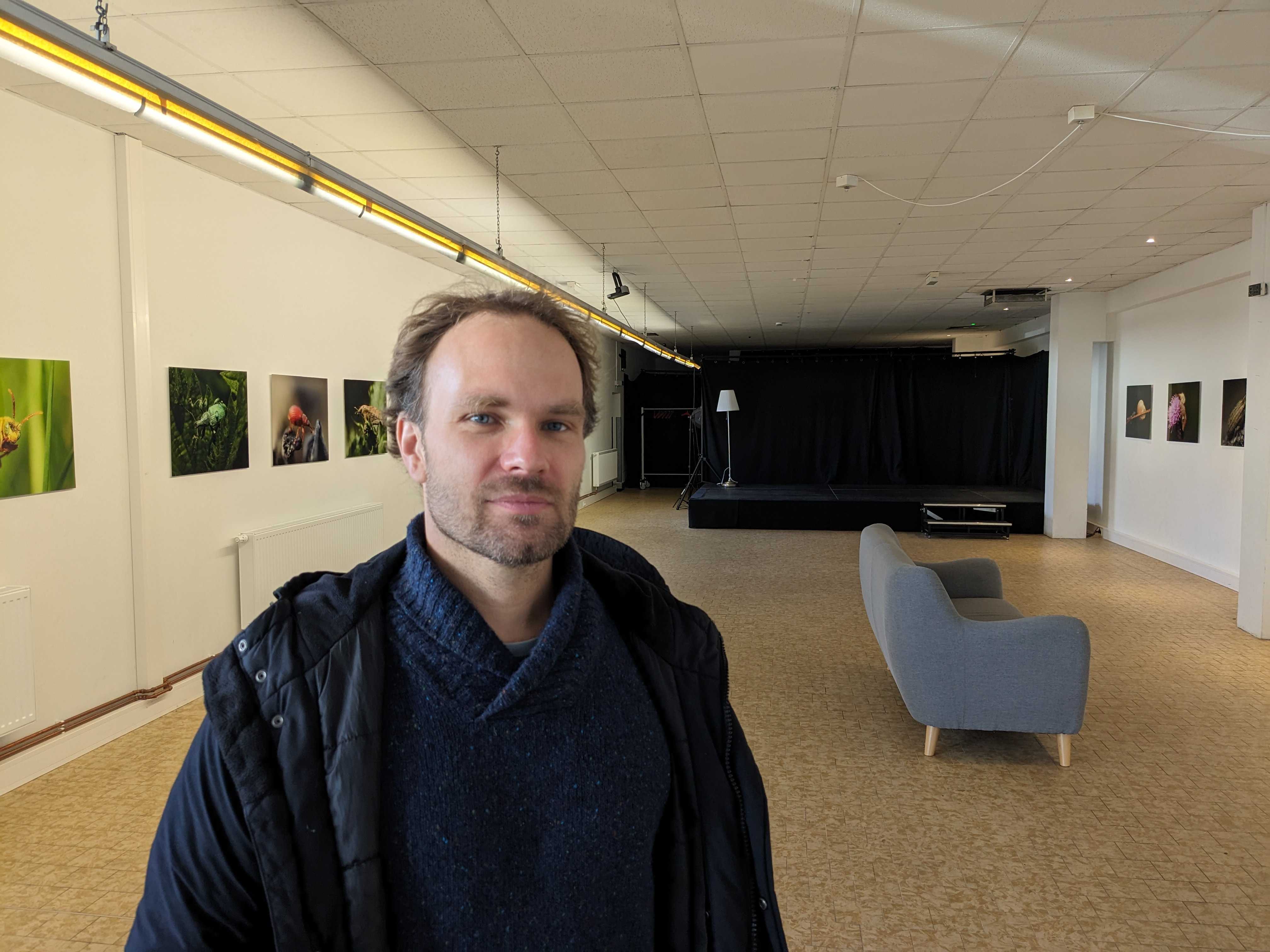 Linus Strothmann (Projektleiter) im Veranstaltungsort für den anstehenden Wahlkreistag in Flensburg. Im Hintergrund ein großer Raum mit Bildern an der Wand und Bühne.